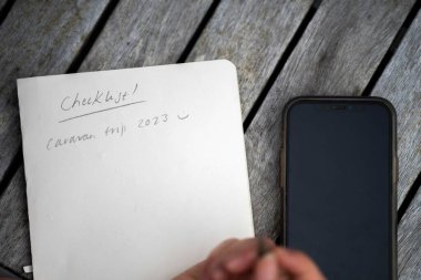 gril writing a camping list in a piece of paper. writing a check list with a pencil in australia