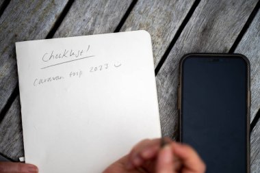 gril writing a camping list in a piece of paper. writing a check list with a pencil in australia