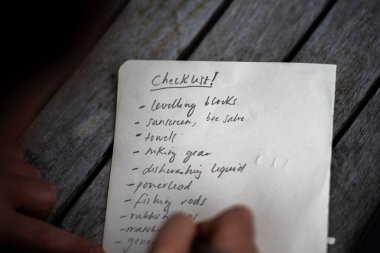 gril writing a camping list in a piece of paper. writing a check list with a pencil and a phone