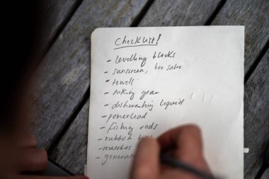 gril writing a camping list in a piece of paper. writing a check list with a pencil and a phone