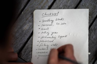 gril writing a camping list in a piece of paper. writing a check list with a pencil and a phone