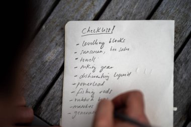 gril writing a camping list in a piece of paper. writing a check list with a pencil and a phone