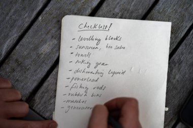 gril writing a camping list in a piece of paper. writing a check list with a pencil and a phone