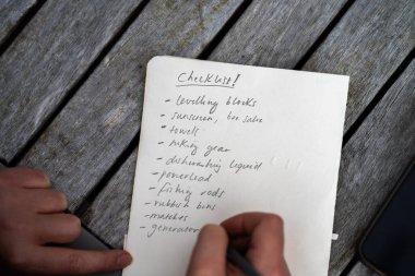 gril writing a camping list in a piece of paper. writing a check list with a pencil and a phone