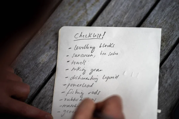 gril writing a camping list in a piece of paper. writing a check list with a pencil and a phone