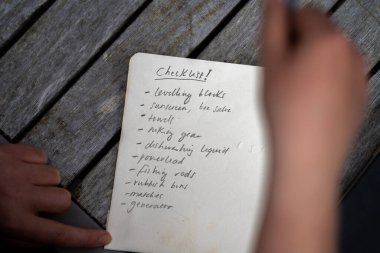 gril writing a camping list in a piece of paper. writing a check list with a pencil and a phone