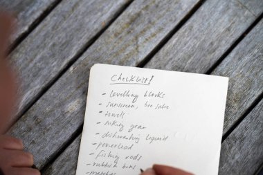 gril writing a camping list in a piece of paper. writing a check list with a pencil and a phone