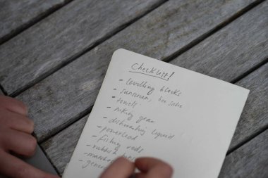 gril writing a camping list in a piece of paper. writing a check list with a pencil and a phone
