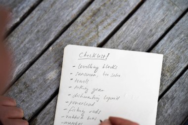 gril writing a camping list in a piece of paper. writing a check list with a pencil and a phone