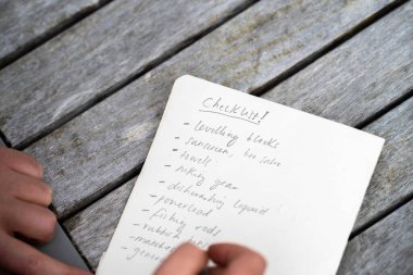 gril writing a camping list in a piece of paper. writing a check list with a pencil and a phone