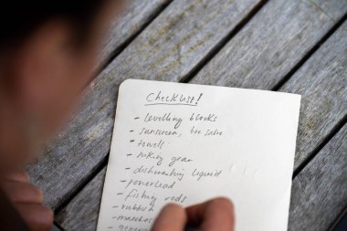 gril writing a camping list in a piece of paper. writing a check list with a pencil and a phone