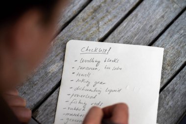 gril writing a camping list in a piece of paper. writing a check list with a pencil and a phone