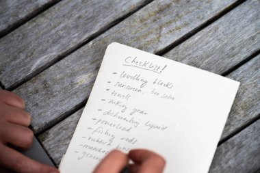 gril writing a camping list in a piece of paper. writing a check list with a pencil and a phone