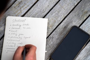 gril writing a camping list in a piece of paper. writing a check list with a pencil and a phone