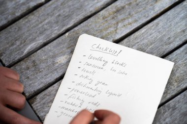 gril writing a camping list in a piece of paper. writing a check list with a pencil and a phone