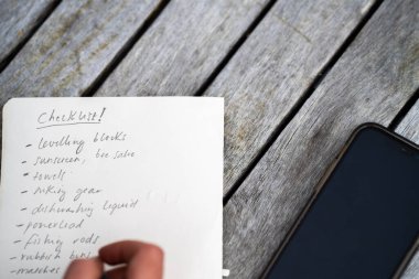 gril writing a camping list in a piece of paper. writing a check list with a pencil and a phone