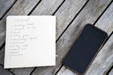gril writing a camping list in a piece of paper. writing a check list with a pencil and a phone