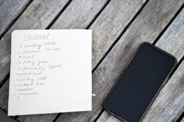 gril writing a camping list in a piece of paper. writing a check list with a pencil and a phone