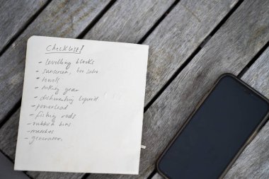 gril writing a camping list in a piece of paper. writing a check list with a pencil and a phone
