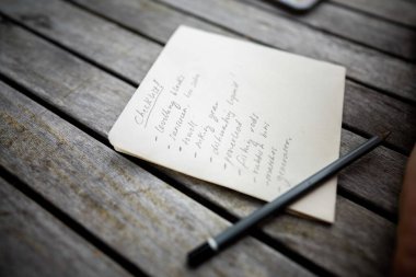 gril writing a camping list in a piece of paper. writing a check list with a pencil and a phone