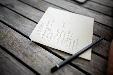 gril writing a camping list in a piece of paper. writing a check list with a pencil and a phone
