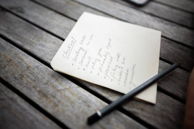 gril writing a camping list in a piece of paper. writing a check list with a pencil and a phone