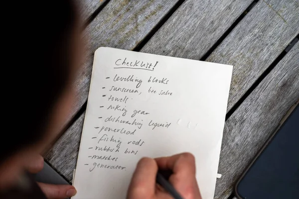 gril writing a camping list in a piece of paper. writing a check list with a pencil and a phone