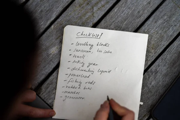 gril writing a camping list in a piece of paper. writing a check list with a pencil and a phone