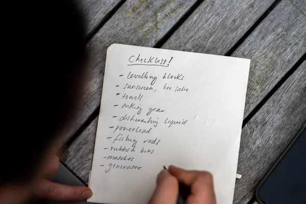 gril writing a camping list in a piece of paper. writing a check list with a pencil and a phone