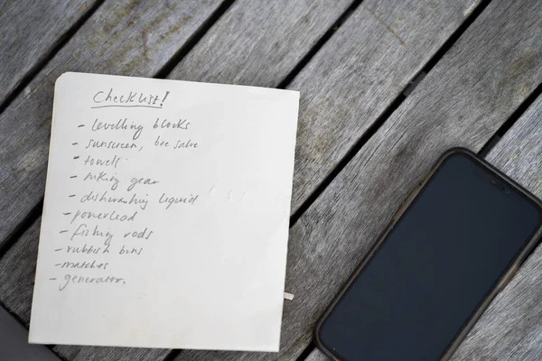 gril writing a camping list in a piece of paper. writing a check list with a pencil and a phone