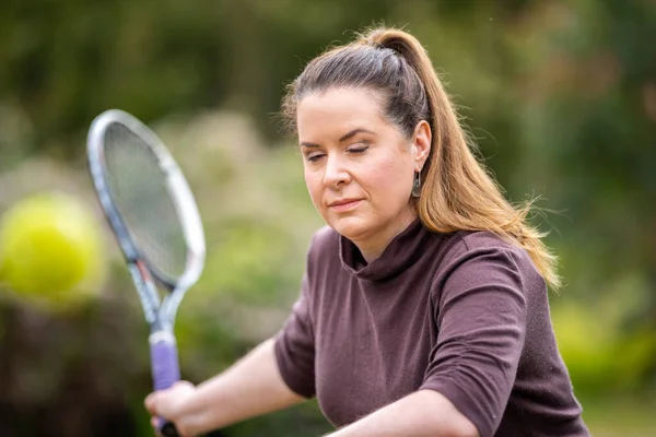 female tennis player practicing forehands and hitting tennis balls on a grass court in england