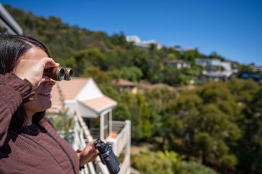 Girl using binoculars on a balcony in a city next to the sea, seaside town in hobart AUSTRALIA bird watching