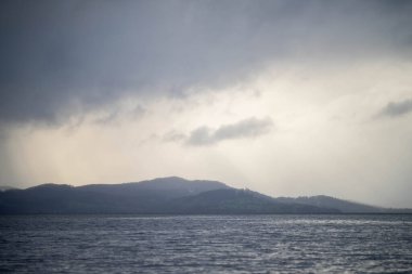 Suyun üzerindeki yumuşak, güzel ışınlar bulutların arasından şafak vakti bir adanın üzerinde pembe bulutların altında ve okyanusun altında