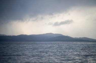Suyun üzerindeki yumuşak, güzel ışınlar bulutların arasından şafak vakti bir adanın üzerinde pembe bulutların altında ve okyanusun altında