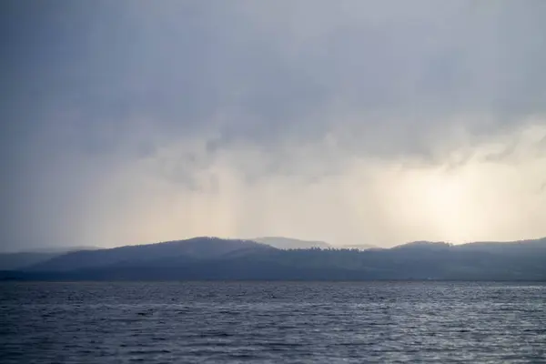 黎明时分 淡淡的美丽光芒掠过水面 穿过岛上的云彩 伴随着粉色的云彩和下方的大海 — 图库照片