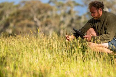 toprak bilimci çiftçi baharda bir tarlada toprak örneklerine ve çimenlere bakıyor. İlkbaharda bitkilerin ve toprak sağlığının büyümesine bakmak