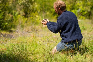 toprak bilimci çiftçi baharda bir tarlada toprak örneklerine ve çimenlere bakıyor. İlkbaharda bitkilerin ve toprak sağlığının büyümesine bakmak
