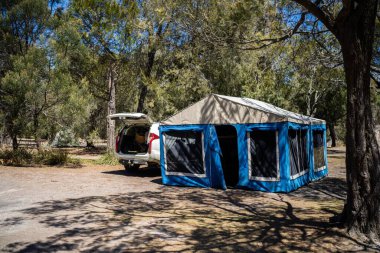 İzole edilmiş bir kamp alanında kamp yapan mavi çadırlı çadırlar ve karavanlar.