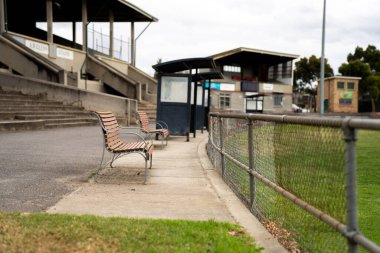 Güneşli bir bahar gününde futbol spor ovalı etrafında park bankları ve koltuklar. Formda kalmak için spor yapan insanlar.