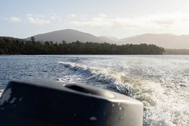 tinny dinghy boat on the water making a wake behind a boat making waves on a river in a national park in australia. beach in summer, dingy going fast in the wilderness clipart