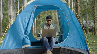 the man using laptop for working while outdoor camping