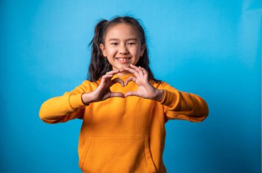 Stüdyoda, kalp sembolünü elleriyle gösteren kızın portresi.