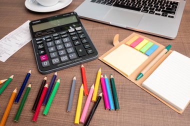 Boş bir defter, bir bilgisayar klavyesi ve çeşitli ofis malzemeleriyle süslenmiş beyaz bir ofis masasının üst görüntüsü. Bu düz konum, modern bir çalışma alanında yaratıcılığı ve verimliliği teşvik eden geniş bir kopya alanı sunar..
