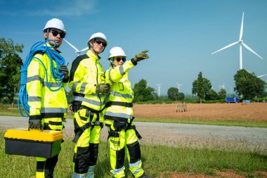 Güvenlik teçhizatı kullanan bir mühendis yenilenebilir enerji alanındaki rüzgar türbininin tabanını yakından inceler..