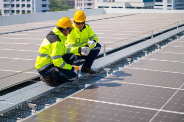 Fabrika çatısındaki güneş panellerini denetleyen teknisyen. Güvenlik donanımı takan bir mühendis, fabrikanın çatısına kurulmuş güneş panelleri üzerinde bakım yapıyor ve en uygun enerji verimliliğini sağlıyor..