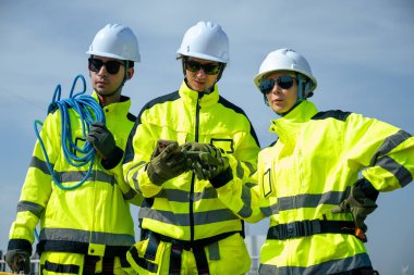 Güvenlik teçhizatı kullanan bir mühendis yenilenebilir enerji alanındaki rüzgar türbininin tabanını yakından inceler..