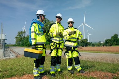 Güvenlik teçhizatı kullanan bir mühendis yenilenebilir enerji alanındaki rüzgar türbininin tabanını yakından inceler..