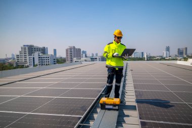 Fabrika çatısındaki güneş panellerini denetleyen teknisyen. Güvenlik donanımı takan bir mühendis, fabrikanın çatısına kurulmuş güneş panelleri üzerinde bakım yapıyor ve en uygun enerji verimliliğini sağlıyor..
