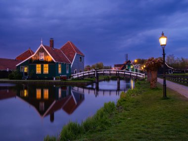 Zaanse Schans, Hollanda - 25 Nisan 2022 alacakaranlıkta, Zaanse Schans 'ın aydınlatılmış binaları su yolu ve köprüye yansıyarak güzel bir gece manzarası yarattılar..