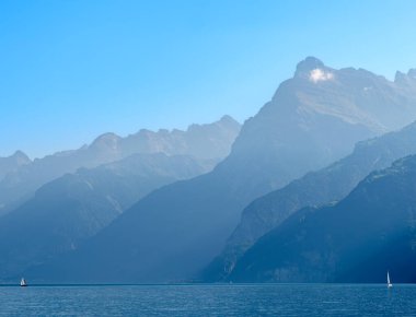 Gündüz sisli ışıkta İsviçre Gölü 'nün kenarındaki dağların ana hatları. Gölde yelkenliler